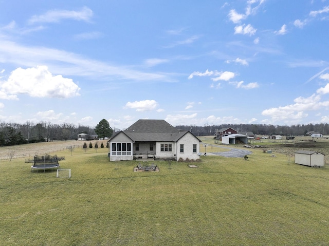 exterior space featuring a rural view, a trampoline, a sunroom, a yard, and an outdoor structure