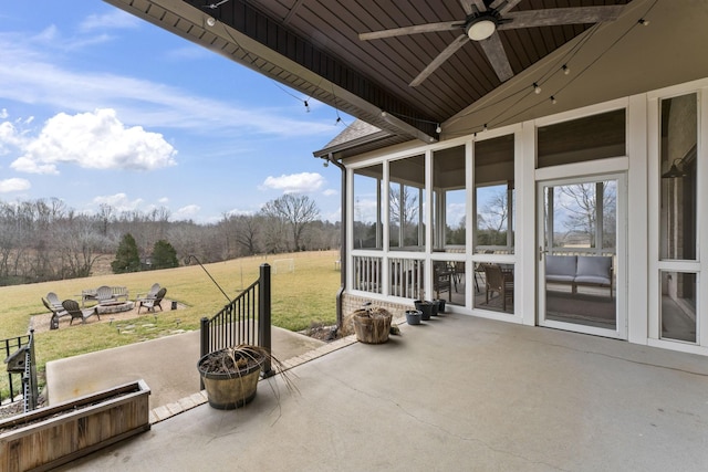 view of patio featuring a fire pit, ceiling fan, and a sunroom