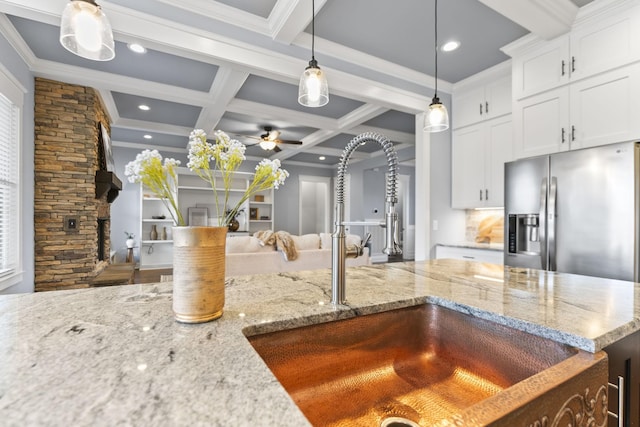 kitchen featuring a stone fireplace, beamed ceiling, stainless steel refrigerator with ice dispenser, and a sink