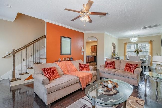 living room with ceiling fan with notable chandelier, dark wood-type flooring, ornamental molding, and a textured ceiling