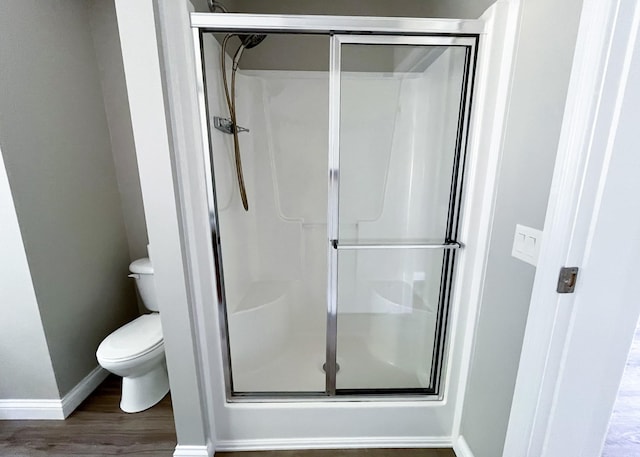 full bathroom featuring baseboards, wood finished floors, toilet, and a stall shower