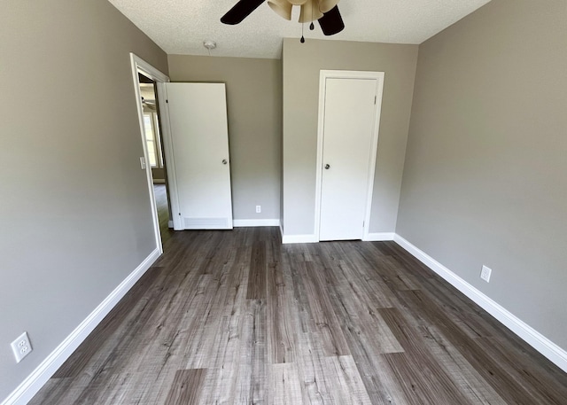 unfurnished bedroom with a textured ceiling, dark wood-type flooring, baseboards, and a ceiling fan