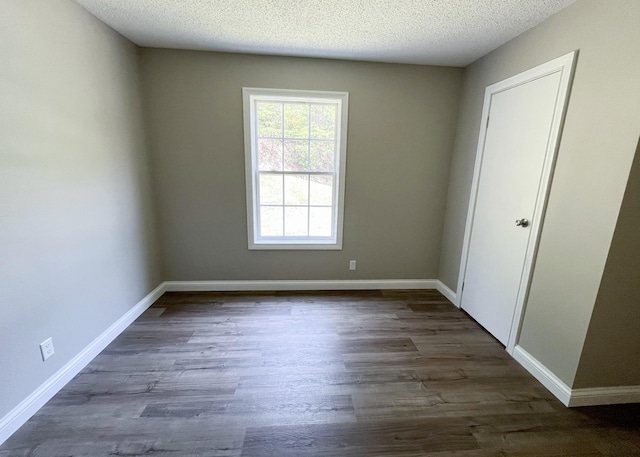 empty room with baseboards, dark wood-type flooring, and a textured ceiling