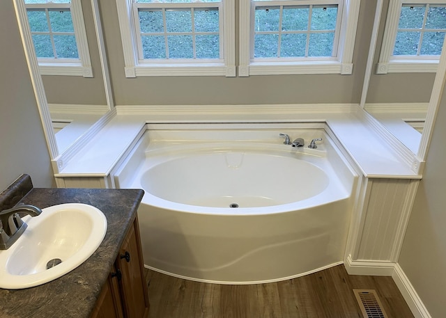 full bath featuring visible vents, vanity, a garden tub, and wood finished floors