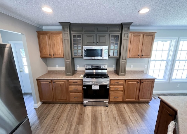 kitchen with crown molding, light wood-style flooring, glass insert cabinets, and stainless steel appliances