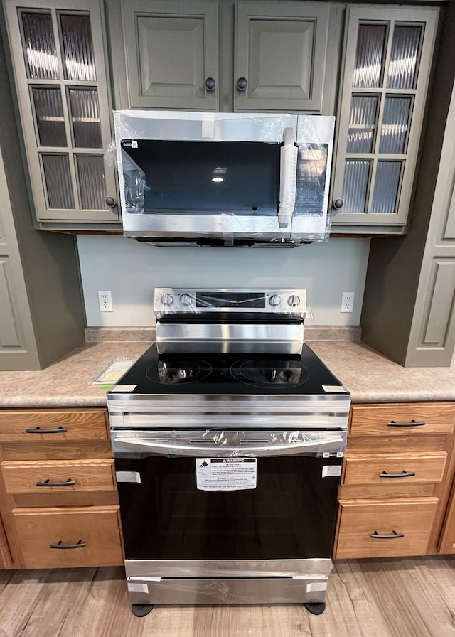 kitchen featuring light wood-type flooring, glass insert cabinets, appliances with stainless steel finishes, and light countertops