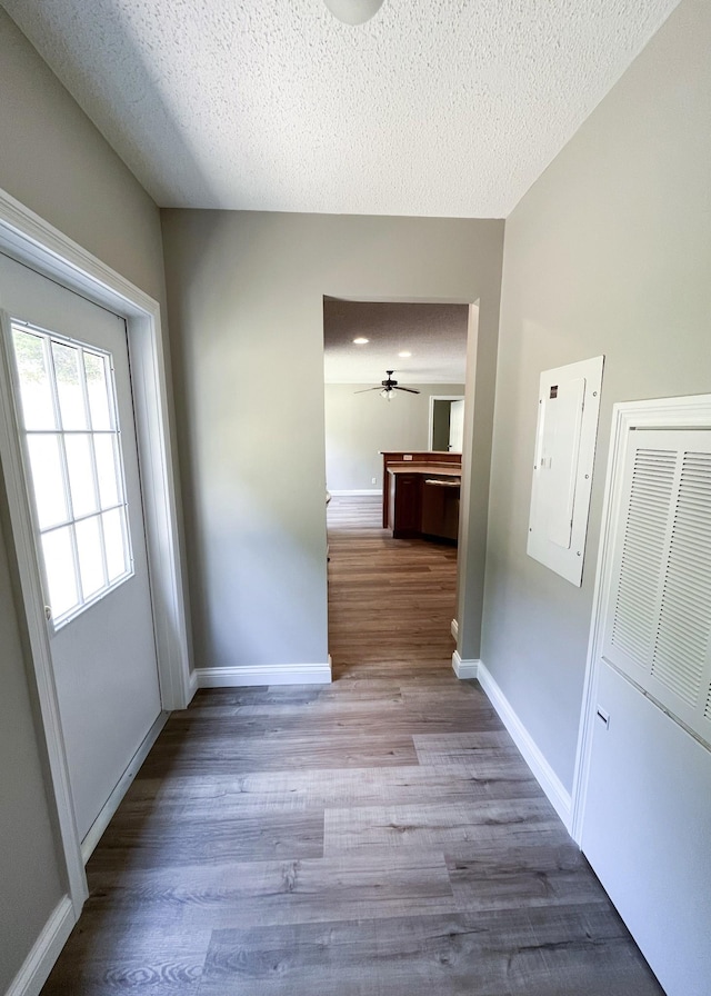 hall featuring electric panel, wood finished floors, baseboards, and a textured ceiling