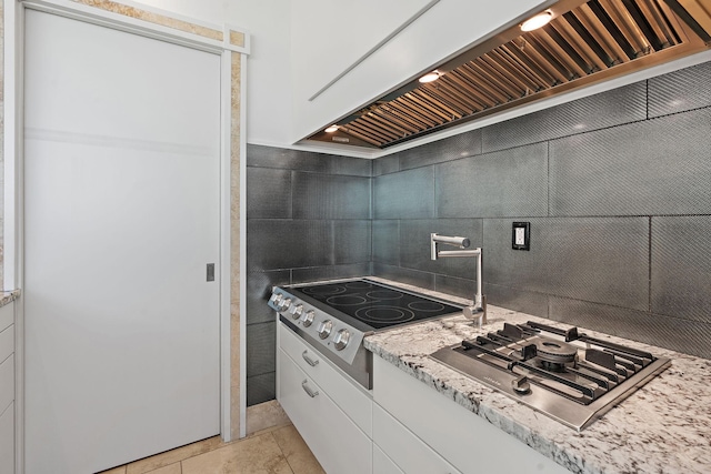 kitchen with wall chimney exhaust hood, stovetop, white cabinetry, light stone counters, and stainless steel gas stovetop