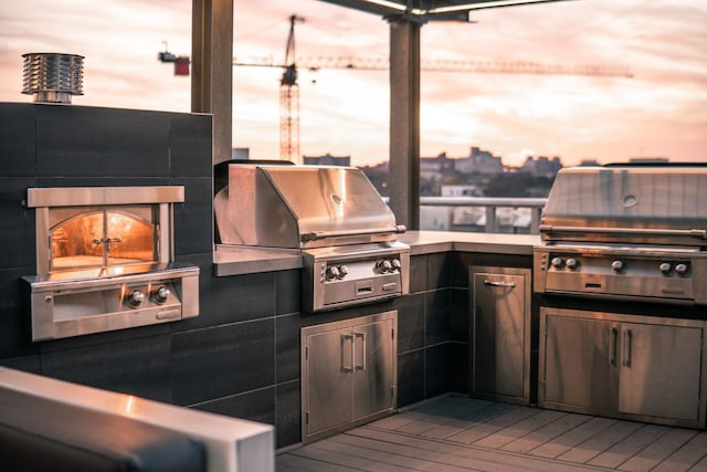 patio terrace at dusk featuring area for grilling and a fireplace