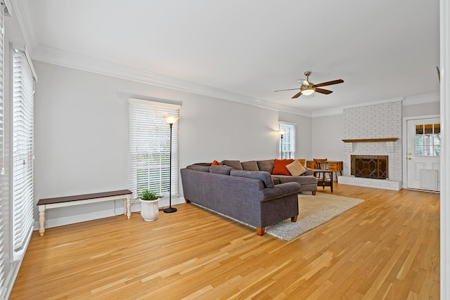 living room with a brick fireplace, ornamental molding, light hardwood / wood-style floors, and ceiling fan