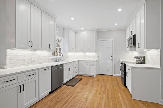 kitchen with tasteful backsplash, white cabinetry, sink, stainless steel appliances, and light hardwood / wood-style flooring