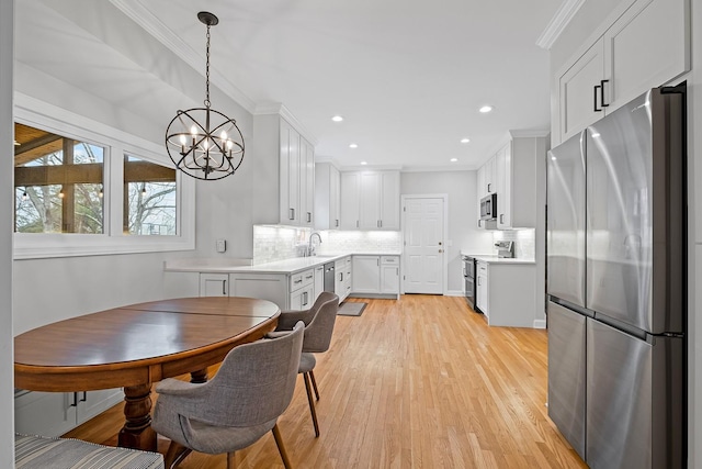 kitchen featuring appliances with stainless steel finishes, pendant lighting, sink, white cabinets, and ornamental molding