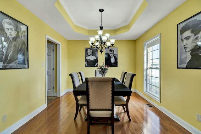 dining area featuring a raised ceiling, ornamental molding, hardwood / wood-style floors, and an inviting chandelier