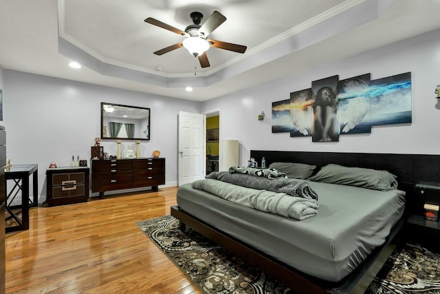 bedroom featuring a raised ceiling, crown molding, ceiling fan, and light wood-type flooring