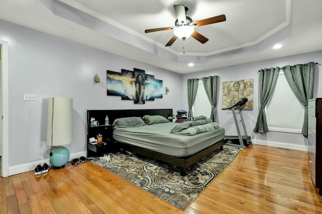 bedroom featuring hardwood / wood-style flooring, ornamental molding, ceiling fan, and a tray ceiling