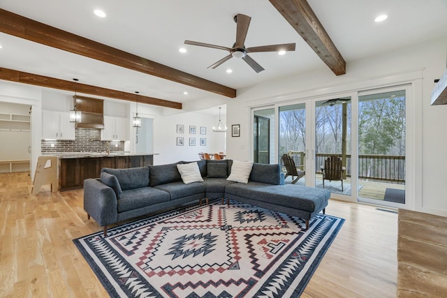 living room with beamed ceiling, ceiling fan with notable chandelier, and light hardwood / wood-style floors