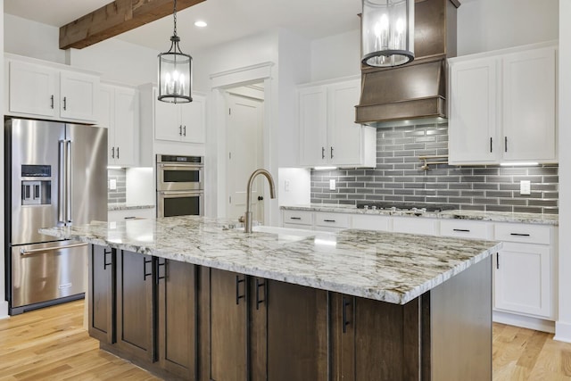 kitchen with appliances with stainless steel finishes, a center island with sink, and white cabinets