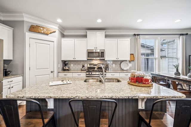 kitchen featuring appliances with stainless steel finishes, white cabinetry, a breakfast bar area, a kitchen island with sink, and light stone counters