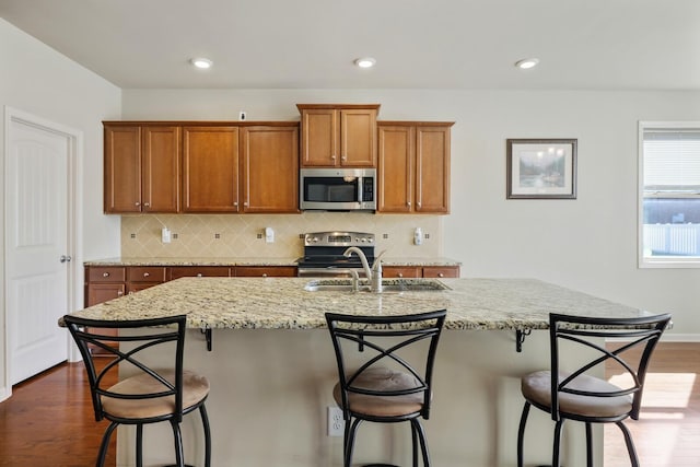 kitchen with appliances with stainless steel finishes, a kitchen breakfast bar, dark hardwood / wood-style flooring, an island with sink, and decorative backsplash