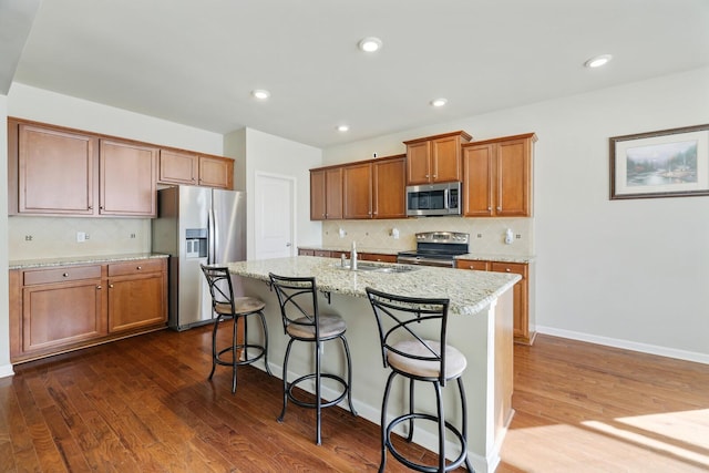 kitchen featuring sink, a kitchen breakfast bar, an island with sink, stainless steel appliances, and light stone countertops