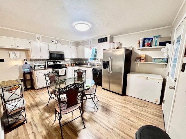 kitchen with appliances with stainless steel finishes, tasteful backsplash, sink, white cabinets, and light hardwood / wood-style flooring