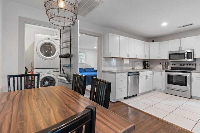 kitchen featuring appliances with stainless steel finishes, stacked washing maching and dryer, and white cabinets