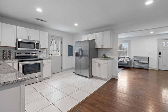 kitchen with white cabinetry, stainless steel appliances, light stone countertops, and light wood-type flooring