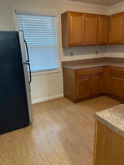 kitchen featuring light hardwood / wood-style floors, ornamental molding, and stainless steel refrigerator