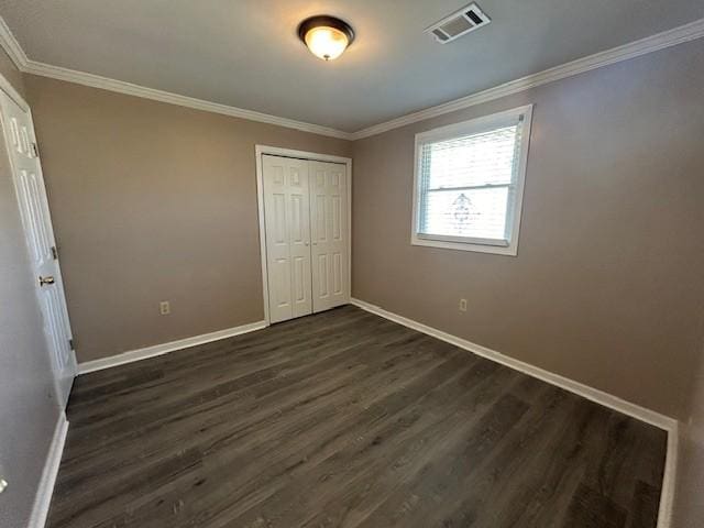 unfurnished bedroom featuring dark wood-type flooring, ornamental molding, and a closet