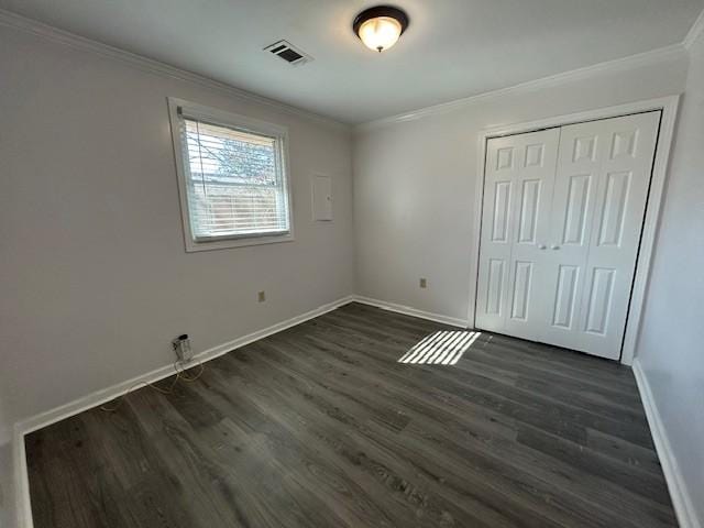 unfurnished bedroom featuring dark wood-type flooring, ornamental molding, and a closet