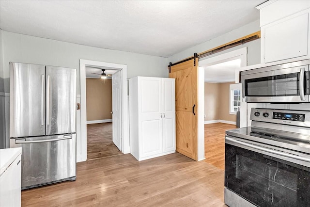 kitchen featuring white cabinetry, light hardwood / wood-style floors, stainless steel appliances, and a barn door