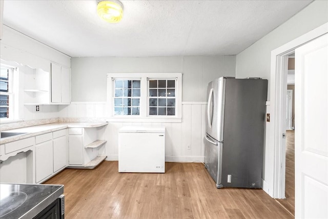 kitchen with light wood-type flooring, stainless steel fridge, white cabinets, and refrigerator