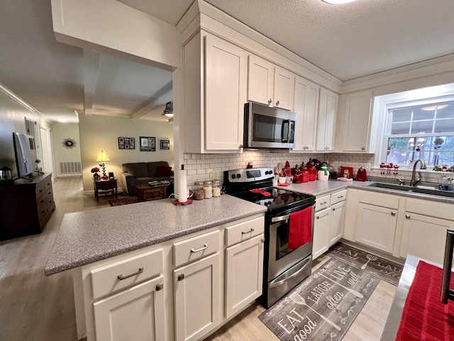 kitchen featuring sink, appliances with stainless steel finishes, white cabinetry, backsplash, and kitchen peninsula