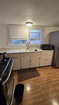 kitchen with light wood-type flooring, stainless steel range, sink, and white cabinets