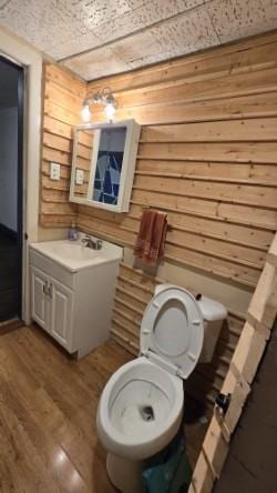 bathroom featuring hardwood / wood-style flooring, toilet, vanity, and wood walls