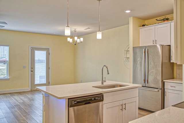 kitchen with sink, appliances with stainless steel finishes, white cabinets, decorative light fixtures, and light wood-type flooring