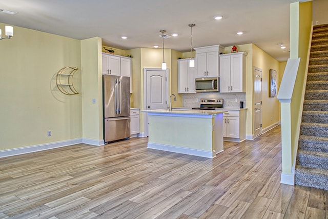 kitchen featuring white cabinetry, stainless steel appliances, decorative light fixtures, and a center island with sink