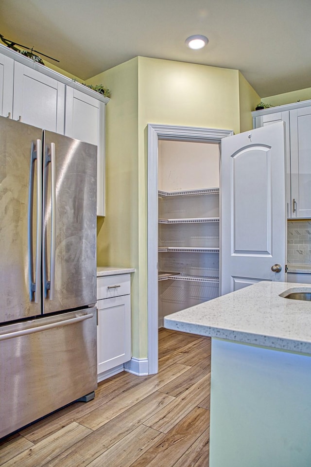 kitchen with white cabinets, light stone counters, stainless steel fridge, and light wood-type flooring