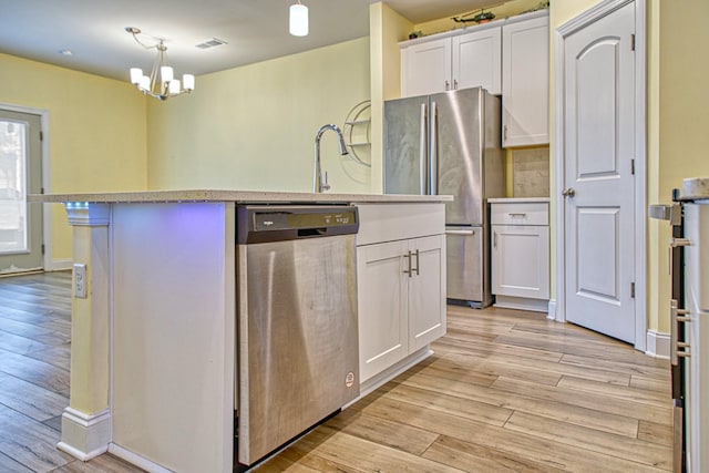 kitchen with white cabinetry, decorative light fixtures, appliances with stainless steel finishes, an island with sink, and light hardwood / wood-style floors