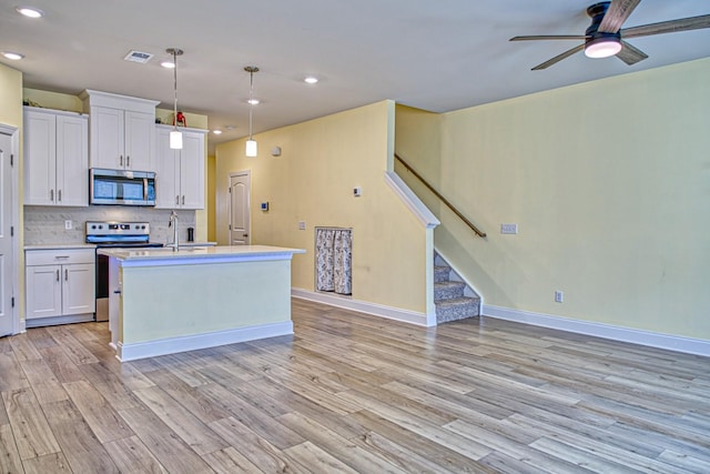 kitchen with pendant lighting, stainless steel appliances, a kitchen island with sink, and white cabinets