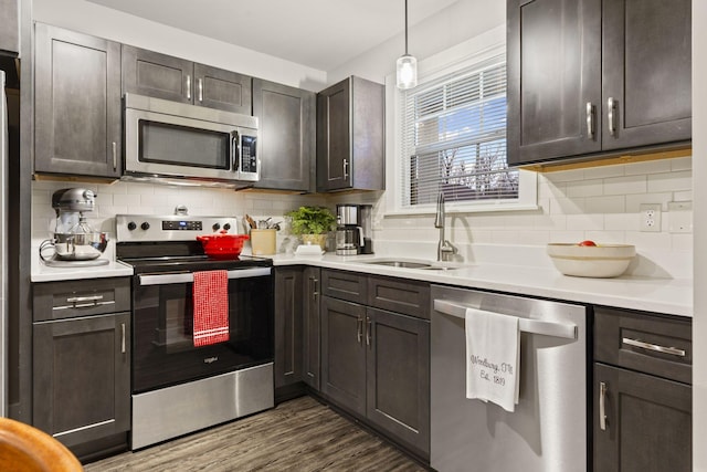 kitchen with decorative light fixtures, sink, dark brown cabinetry, stainless steel appliances, and dark wood-type flooring