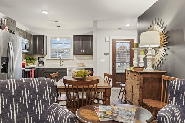 kitchen featuring sink, stainless steel appliances, dark brown cabinetry, decorative backsplash, and decorative light fixtures