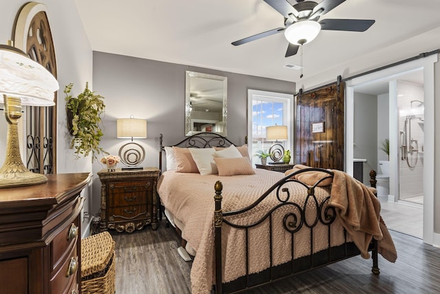 bedroom featuring connected bathroom, dark hardwood / wood-style floors, a barn door, and ceiling fan