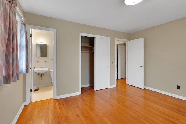 unfurnished bedroom featuring ensuite bathroom, sink, light wood-type flooring, and a closet