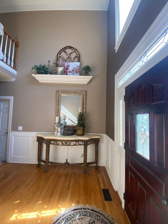 foyer with wainscoting, wood finished floors, visible vents, and crown molding