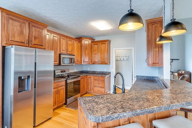 kitchen featuring a breakfast bar, decorative light fixtures, light hardwood / wood-style flooring, appliances with stainless steel finishes, and kitchen peninsula