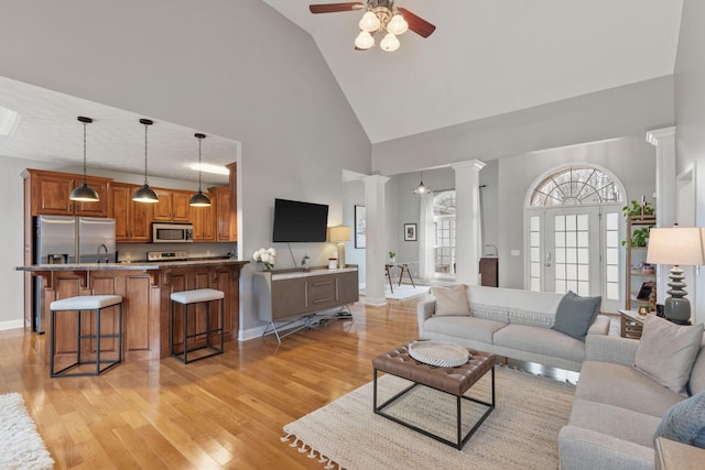 living room featuring high vaulted ceiling, sink, light hardwood / wood-style floors, and ornate columns