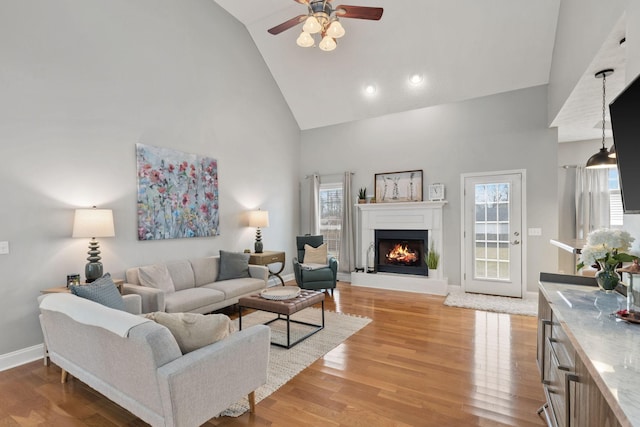 living room featuring ceiling fan, high vaulted ceiling, and light hardwood / wood-style flooring