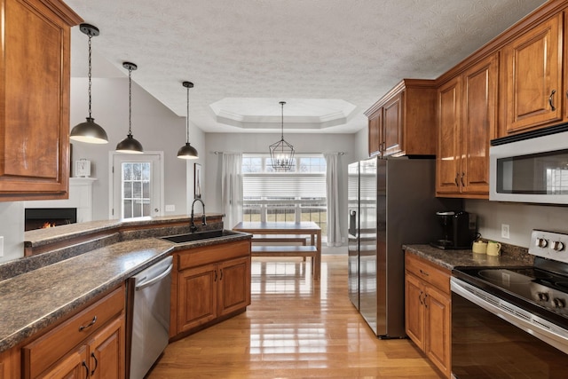 kitchen featuring pendant lighting, sink, a tray ceiling, stainless steel appliances, and light hardwood / wood-style flooring