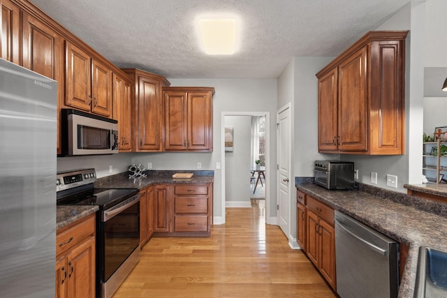 kitchen featuring stainless steel appliances, dark stone countertops, a textured ceiling, and light hardwood / wood-style floors